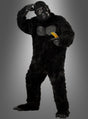 Eine Person in einem Gorilla-Kostüm für Herren in Größe XL steht auf einem Bein, hält in einer Hand eine Banane und berührt mit der anderen ihren Kopf, vor einem grauen Hintergrund mit Farbverlauf.