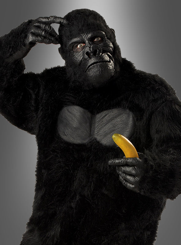Eine Person, die das Gorilla-Kostüm für Herren in Größe XL trägt, kratzt sich am Kopf und zeigt auf eine Banane, während sie vor einem schlichten Hintergrund mit Farbverlauf steht.