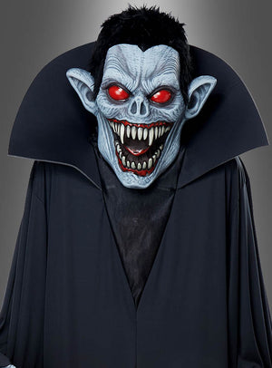 Eine Person im „Gigantischen Vampir-Kostüm“ oder als Dekoration, ca. 240 cm groß, mit einer blauhäutigen Vampirmaske mit rot leuchtenden Augen, spitzen Ohren, scharfen Zähnen und einem schwarzen Umhang mit hohem Kragen – ein wahrhaft beeindruckendes Halloween-Kostüm, das sich perfekt für jede Halloween-Feier eignet.