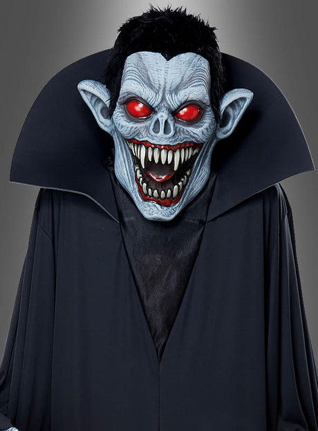 Eine Person im „Gigantischen Vampir-Kostüm“ oder als Dekoration, ca. 240 cm groß, mit einer blauhäutigen Vampirmaske mit rot leuchtenden Augen, spitzen Ohren, scharfen Zähnen und einem schwarzen Umhang mit hohem Kragen – ein wahrhaft beeindruckendes Halloween-Kostüm, das sich perfekt für jede Halloween-Feier eignet.