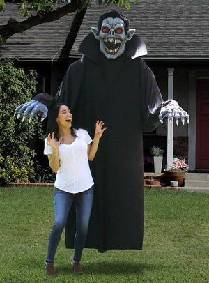 Eine Frau reagiert überrascht, als sie vor einer großen, bedrohlich wirkenden Vampir-Dekoration in einem Garten steht, bei der es sich um das „Gigantisches Vampir-Kostüm oder Deko ca. 240 cm“ handelt – perfekt für jede Halloween-Verkleidung.