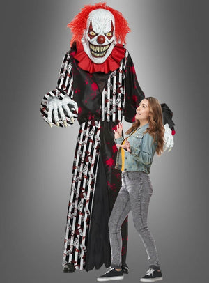 Eine imposante Gestalt im „Gigantischen Horrorclown-Kostüm oder Deko, ca. 240 cm“ – komplett mit wildem rotem Haar und messerscharfen Zähnen – ragt bedrohlich über einer erschrockenen jungen Frau in Freizeitkleidung vor einem grauen Hintergrund empor und ist damit die perfekte Halloween-Dekoration, um eine gruselige Szene zu schaffen.