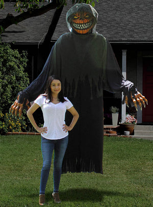 Eine Frau steht vor einer großen, auffälligen Halloween-Dekoration auf einem Rasen – einer grinsenden Gestalt mit Kapuze, die genau wie das „Horror-Kürbis-Kostüm oder -Dekoration, ca. 240 cm“ aussieht.