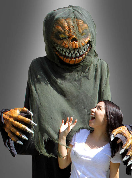 Eine Frau in einem weißen Hemd lächelt und posiert spielerisch neben einer großen Person, die das „Horror Kürbis Kostüm oder Deko ca. 240 cm“ trägt – ein zerfetztes, monströses Kostüm mit großen Klauen und scharfen Zähnen –, vor einem grauen Hintergrund.