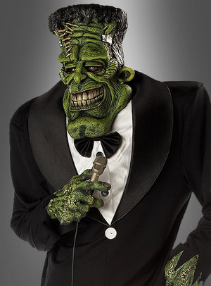 Im „Big Franky Monsterkostüm mit übergroßer Maske“ hält eine Person mit einer grünen Frankenstein-Monster-Maske und einem entsprechenden Kostüm ein Mikrofon in der Hand; sie trägt einen schwarzen Smoking mit Fliege vor einem grauen Hintergrund – perfekt für jede Themenveranstaltung und erhältlich in den Herrengrößen L–XL.
