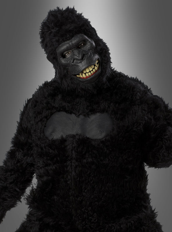 Eine Person, die ein schwarzes Gorilla-Kostüm mit beweglicher Ani-Motion-Maske trägt, bei der menschliche Augen und Zähne zu sehen sind, steht vor einem grauen Hintergrund mit Farbverlauf. Dieses beeindruckende Gorilla-Kostüm mit beweglicher Ani-Motion-Maske eignet sich perfekt als Highlight unter den Tierkostümen für den Karneval und jede Feier.