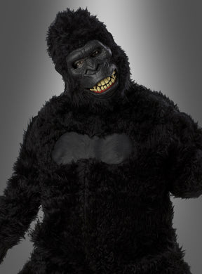 Eine Person, die ein schwarzes Gorilla-Kostüm mit beweglicher Ani-Motion-Maske trägt, bei der menschliche Augen und Zähne zu sehen sind, steht vor einem grauen Hintergrund mit Farbverlauf. Dieses beeindruckende Gorilla-Kostüm mit beweglicher Ani-Motion-Maske eignet sich perfekt als Highlight unter den Tierkostümen für den Karneval und jede Feier.