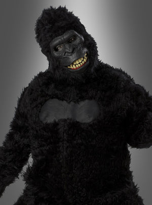 Eine Person, die ein schwarzes Gorilla-Kostüm mit beweglicher Ani-Motion-Maske trägt, bei der menschliche Augen und Zähne zu sehen sind, steht vor einem grauen Hintergrund mit Farbverlauf. Dieses beeindruckende Gorilla-Kostüm mit beweglicher Ani-Motion-Maske eignet sich perfekt als Highlight unter den Tierkostümen für den Karneval und jede Feier.