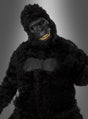 Eine Person, die ein schwarzes Gorilla-Kostüm mit beweglicher Ani-Motion-Maske trägt, bei der menschliche Augen und Zähne zu sehen sind, steht vor einem grauen Hintergrund mit Farbverlauf. Dieses beeindruckende Gorilla-Kostüm mit beweglicher Ani-Motion-Maske eignet sich perfekt als Highlight unter den Tierkostümen für den Karneval und jede Feier.