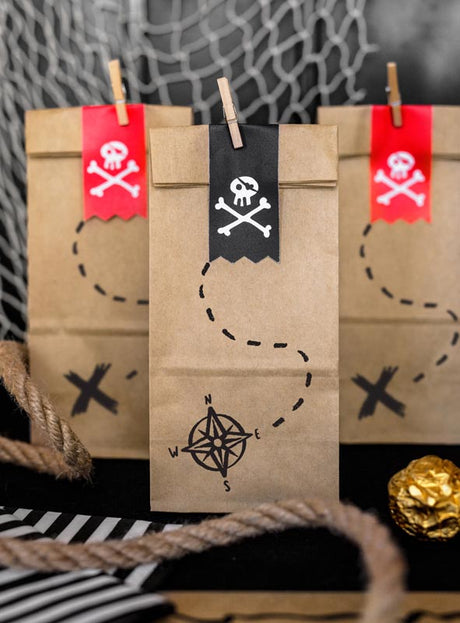 Im Set sind sechs braune Papier-„Geschenktüten Piratenparty“ enthalten, die jeweils mit Piratenmotiven wie Totenkopf-Aufklebern und Schatzkarten-Motiven verziert sind. Im Vordergrund sind Seile und goldverpackte Schokoladenmünzen zu sehen – diese Tüten eignen sich ideal als umweltfreundliche Geschenktüten für eine aufregende Piratenparty zum Kindergeburtstag.