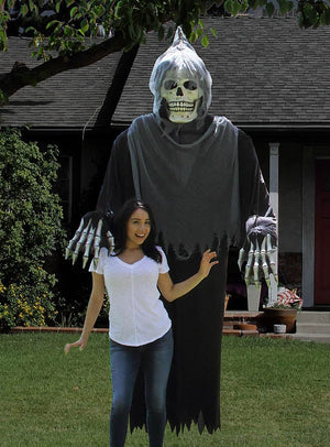 Eine Frau posiert lächelnd vor einer „Gigantischer Tod“-Kostüm- oder Dekoration – einem 240 cm großen Skelett als Halloween-Dekoration – auf dem Rasen vor einem Haus.