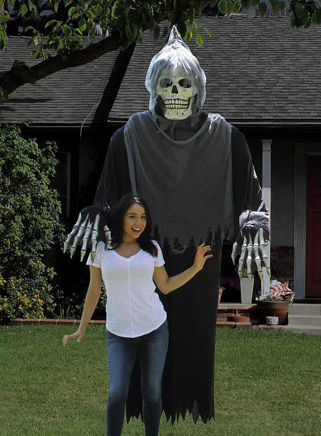 Eine Frau posiert lächelnd vor einer „Gigantischer Tod“-Kostüm- oder Dekoration – einem 240 cm großen Skelett als Halloween-Dekoration – auf dem Rasen vor einem Haus.