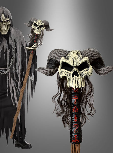 Eine Person in einem Kapuzenmantel hält den „Hexenmeister-Dolch mit Hörnern“ (140 cm) in der Hand, dessen Griff mit einem gehörnten Totenkopf mit dunklem Haar und roten Symbolen verziert ist, der sich vor einem schlichten grauen Hintergrund abhebt.