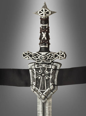 Das „Ritterschwert mit Gürtel, 60 cm“ ist ein Schwert im mittelalterlichen Stil mit einem kunstvoll verzierten Griff, der mit keltischen Knotenmustern, einem Totenkopf und einer dekorativen Parierstange verziert ist – perfekt für jedes Mittelalterkostüm oder jede Karnevalsveranstaltung – und wurde vor einem grauen Hintergrund mit Farbverlauf fotografiert.