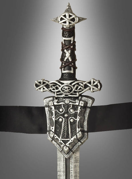 Das „Ritterschwert mit Gürtel, 60 cm“ ist ein Schwert im mittelalterlichen Stil mit einem kunstvoll verzierten Griff, der mit keltischen Knotenmustern, einem Totenkopf und einer dekorativen Parierstange verziert ist – perfekt für jedes Mittelalterkostüm oder jede Karnevalsveranstaltung – und wurde vor einem grauen Hintergrund mit Farbverlauf fotografiert.
