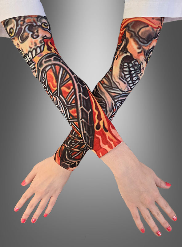 Zwei verschränkte Arme mit realistisch gestalteten Tattoo-Armstulpen im Skelett-Design, verziert mit Totenkopf- und Flammenmotiven, deren Hände sorgfältig manikürte Nägel aufweisen, vor einem grauen Hintergrund mit Farbverlauf.