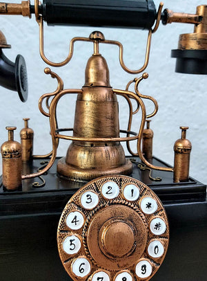 Nahaufnahme des antiken Dekorationsrequisits „Telefon der 20er Jahre“ mit Messingoptik, bei der das nummerierte Wählrad und der Hörer vor einem strukturierten weißen Hintergrund besonders gut zur Geltung kommen – ein perfektes Stück für die Vintage-Dekoration.