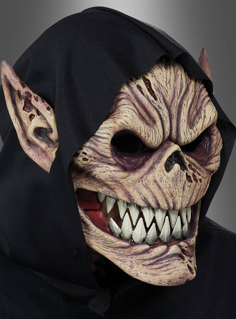 Eine Person, die eine „Kobold Dämon Ani-Motion“-Maske mit scharfen Zähnen, spitzen Ohren und einer schwarzen Kapuze trägt, vor einem schlichten grauen Hintergrund.