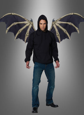 Vor einem schlichten Hintergrund mit Farbverlauf steht ein Mann in einem schwarzen Kapuzenpulli und blauen Jeans, an dessen Rücken große Dämonen-Skelettflügel befestigt sind – ein auffälliges Halloween-Cosplay.