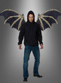 Vor einem schlichten Hintergrund mit Farbverlauf steht ein Mann in einem schwarzen Kapuzenpulli und blauen Jeans, an dessen Rücken große Dämonen-Skelettflügel befestigt sind – ein auffälliges Halloween-Cosplay.