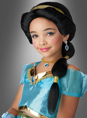 Ein junges Mädchen trägt ein blau-goldenes „Wüstenprinzessin“-Kostüm mit Schmuck, eine gestylte Frisur unter einer „Arabische Prinzessin“-Kinderperücke und ein dezentes Make-up und posiert vor einem schlichten grauen Hintergrund.