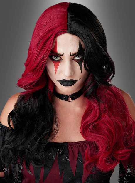 Model mit rot-schwarzem, im Mittelscheitel getrennten Haar, gestylt mit einer auffälligen rot-schwarzen „Jester“-Perücke für Damen, dramatischem schwarz-rotem Clown-Make-up, dunklem Lippenstift und einem mit Nieten besetzten Halsband, das ein schwarz-rotes, schulterfreies Oberteil vor grauem Hintergrund trägt.