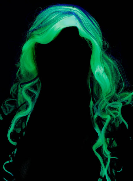 Die Silhouette einer Person mit langen, welligen Haaren, die im Dunkeln hellgrün leuchten, vor schwarzem Hintergrund, vermittelt den geheimnisvollen Reiz der „Leuchtende Lockenperücke Geisterfrau“.