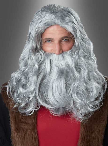 Eine Person mit der „Grauen Perücke und Bart Da Vinci“ – lang und wellig frisiert – trägt ein rotes Hemd und eine braune Weste und steht vor einem neutralen grauen Hintergrund.