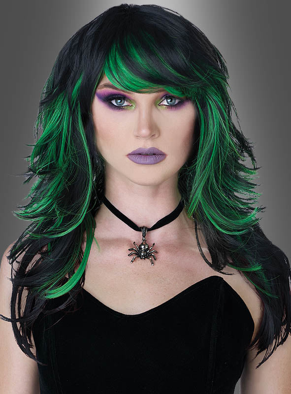 Eine Person mit welligem schwarz-grünem Haar, das zu einer Kräuterhexe-Perücke mit grünen Strähnen gestylt ist, mit auffälligem lila Make-up und helllila Lippenstift, gekleidet in ein schwarzes Outfit und eine schwarze Halskette mit Spinnenanhänger – perfekt für ein Hexenkostüm – vor einem grauen Hintergrund.