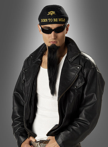 Vor einem grauen Hintergrund steht ein Mann, der eine schwarze Lederjacke, eine Sonnenbrille und eine Kappe mit der Aufschrift „Born to be Wild“ trägt. Seinen klassischen Metal-Look rundet er mit dem unverkennbaren „Cooler Langer Rocker“-Kinnbart ab, der den echten Biker-Bart-Stil verkörpert.