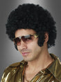 Ein Mann mit einer Afro-Perücke im Stil der 70er Jahre mit Koteletten, einer goldenen Sonnenbrille, einem goldenen Hemd und einer goldenen Halskette verkörpert den kühnen Geist dieser Ära, während er in diesem auffälligen Disco-Outfit vor einem grauen Hintergrund mit Farbverlauf posiert.