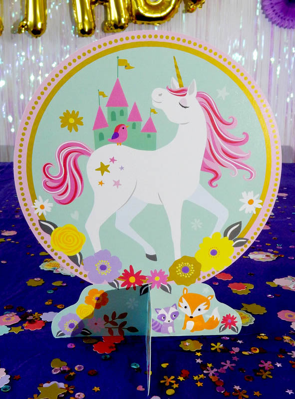 Der Einhorn-Tischdeko-Aufsteller (24,3 cm) zeigt ein farbenfrohes Einhorn mit rosa Mähne, das vor einem Schloss steht, umgeben von Blumen, einem Fuchs, einem Vogel und einer Katze auf einem blauen, mit Konfetti bedeckten Tisch – ein zauberhafter Akzent für jede Einhorn-Geburtstagsparty oder eine bezaubernde Einhorn-Tischdekoration.