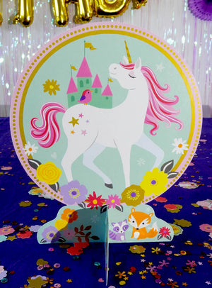 Der Einhorn-Tischdeko-Aufsteller (24,3 cm) zeigt ein farbenfrohes Einhorn mit rosa Mähne, das vor einem Schloss steht, umgeben von Blumen, einem Fuchs, einem Vogel und einer Katze auf einem blauen, mit Konfetti bedeckten Tisch – ein zauberhafter Akzent für jede Einhorn-Geburtstagsparty oder eine bezaubernde Einhorn-Tischdekoration.