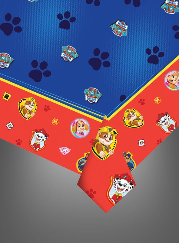 Blaue und rote „Paw Patrol“-Tischdecke mit den Gesichtern der Figuren, Pfotenabdrücken und Logos, an den Ecken teilweise umgeschlagen, auf grauem Hintergrund – perfekt für Ihre nächste „Paw Patrol“-Party.