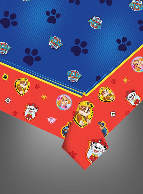 Blaue und rote „Paw Patrol“-Tischdecke mit den Gesichtern der Figuren, Pfotenabdrücken und Logos, an den Ecken teilweise umgeschlagen, auf grauem Hintergrund – perfekt für Ihre nächste „Paw Patrol“-Party.