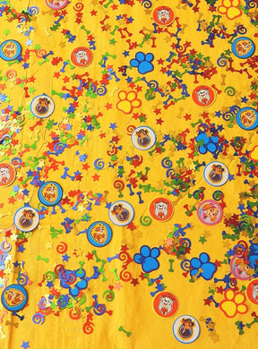 Eine gelbe Fläche, verziert mit bunten Konfetti, Hundepfotenabdrücken und runden Aufklebern mit fröhlichen „Paw Patrol“-Figuren – ideal als „Tischkonfetti Paw Patrol“, um jede ausgelassene „Paw Patrol“-Geburtstagsfeier zu verschönern.