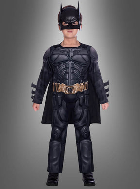 Ein Kind, das das „Batman Dark Knight“-Kostüm für Kinder trägt – mit Maske, Umhang und Werkzeuggürtel –, steht vor einem grauen Hintergrund.
