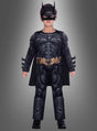 Ein Kind, das das „Batman Dark Knight“-Kostüm für Kinder trägt – mit Maske, Umhang und Werkzeuggürtel –, steht vor einem grauen Hintergrund.
