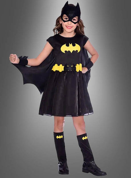 Ein Kind in einem schwarzen Batgirl-Kinderkostüm, bestehend aus einem schwarzen Kleid mit gelbem Fledermaus-Logo, einem schwarzen Umhang, einer Maske, einem gelben Gürtel, schwarzen Stiefeln und passenden Armbändern, steht vor einem grauen Hintergrund. Dieses schwarze Batgirl-Kinderkostüm ist perfekt für kleine Superhelden, die es lieben, sich in ihr Lieblings-Fledermaus-Kostüm zu schlüpfen.