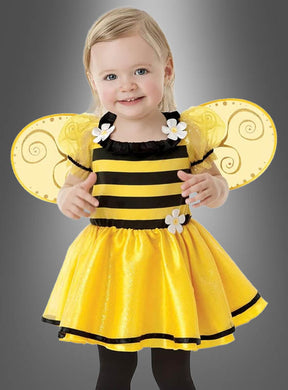 Ein kleines Kind lächelt, während es ein gelb-schwarzes „Biene Kleid und Flügel für Kinder“ mit Flügeln und Blumenverzierungen trägt und vor einem grauen Hintergrund steht.