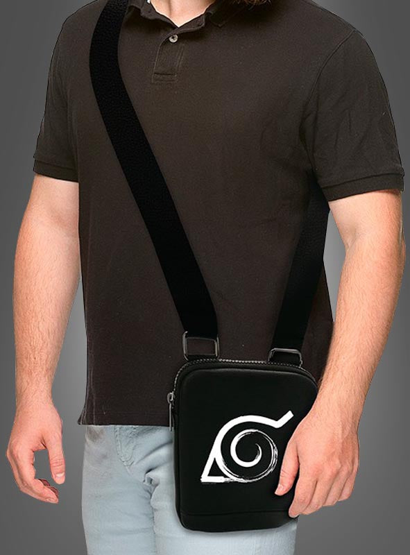 Eine Person in einem schwarzen Poloshirt und einer hellen Hose trägt die Umhängetasche „Naruto schwarz“, auf deren Vorderseite ein auffälliges, stilisiertes weißes Augensymbol zu sehen ist, das an das ikonische Konoha-Symbol erinnert.