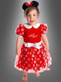 Ein kleines Kind steht barfuß da und trägt ein bezauberndes Minnie-Maus-Kleid aus rotem Stoff mit weißen Punkten sowie ein passendes schwarzes Stirnband mit Mausohren, das mit einer roten Schleife verziert ist. Im Hintergrund ist ein grauer Farbverlauf zu sehen.