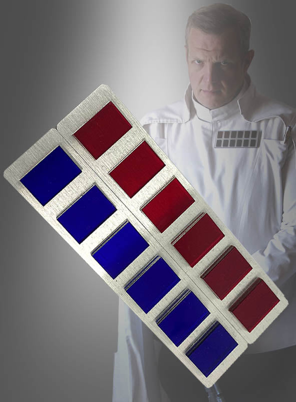 Im Hintergrund steht ein Mann in einer weißen Uniform; im Vordergrund ist ein Metallabzeichen mit roten und blauen rechteckigen Streifen zu sehen, das dem Rangabzeichen von Direktor Orson Krennik ähnelt.