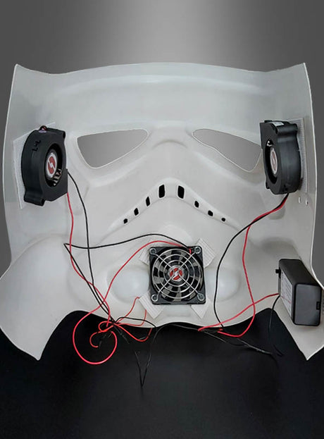 Innenansicht einer weißen Maske mit angebauten Lüftern, Kabeln und einer Stromquelle vor grauem Hintergrund – ideal, um Ihren Cosplay-Helm aufzuwerten oder Star-Wars-Kostümen mit dem Lüftersystem für Masken und Helme zusätzlichen Komfort zu verleihen.