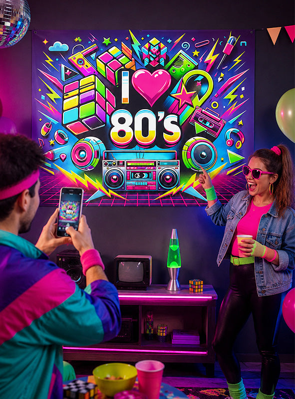 Zwei Personen in Retro-Outfits aus den 1980er Jahren posieren neben einer „I love 80s“-Neonreklame, umgeben von klassischer Partydekoration wie einer Boombox, einer Lavalampe, Rubik-Würfeln, Luftballons und farbenfroher Schwarzlicht-Dekoration. Das große, waschbare UV-Stoffbanner „80er Jahre“ (150 x 185 cm) als Partydekoration sorgt für einen zusätzlichen Farbtupfer und macht dies zur ultimativen Kulisse für eine unvergessliche 80er-Jahre-Party.