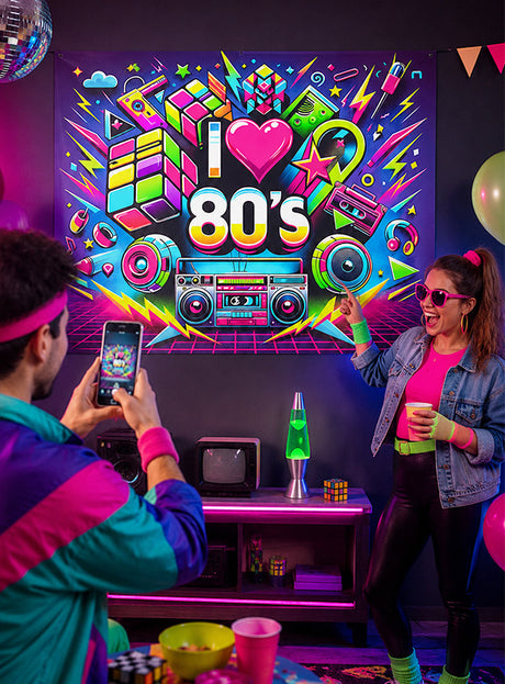 Zwei Personen in Retro-Outfits aus den 1980er Jahren posieren neben einer „I love 80s“-Neonreklame, umgeben von klassischer Partydekoration wie einer Boombox, einer Lavalampe, Rubik-Würfeln, Luftballons und farbenfroher Schwarzlicht-Dekoration. Das große, waschbare UV-Stoffbanner „80er Jahre“ (150 x 185 cm) als Partydekoration sorgt für einen zusätzlichen Farbtupfer und macht dies zur ultimativen Kulisse für eine unvergessliche 80er-Jahre-Party.