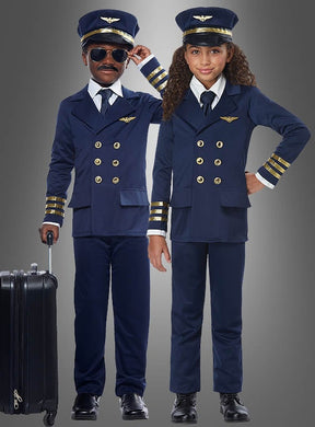 Zwei Kinder, gekleidet in marineblaue Flugzeugkapitän-Kostüme für Kinder, komplett mit den klassischen Pilotenmützen, stehen vor einem grauen Hintergrund neben einem Koffer.