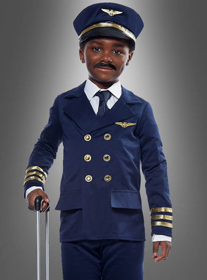 Ein Kind, das ein Flugzeugkapitän-Kostüm für Kinder mit goldenen Knöpfen und Streifen trägt, eine dazu passende Mütze auf dem Kopf hat und den Griff eines Koffers in der Hand hält, steht vor einem grauen Hintergrund.