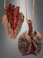 Zwei anatomische Skulpturen – ein detailgetreues Herz und eine aufwendig gearbeitete Lunge – hängen nebeneinander an Schnüren vor einem grauen Hintergrund mit Farbverlauf und sind damit auffällige Deko-Elemente zum Thema „Innereien und Leichenteile“ für Halloween.