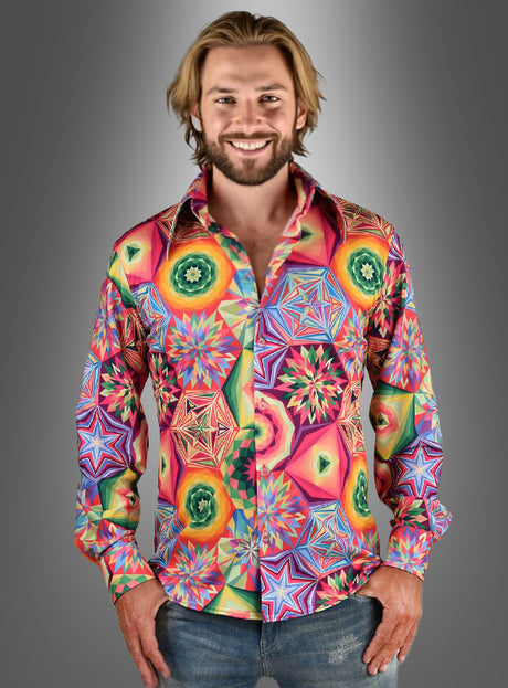Ein Mann mit schulterlangen blonden Haaren trägt das „Funky Neon Hemd Herren“ mit leuchtenden Stern- und Wirbelmustern – perfekt für eine 70er-Jahre-Schlagerparty –, während er vor einem grauen Hintergrund mit Farbverlauf steht.